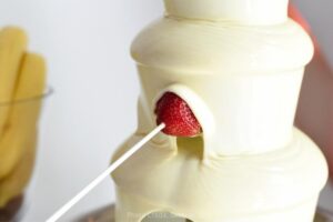 white chocolate fountain with a strawberry on a skewer dipping into the fountain