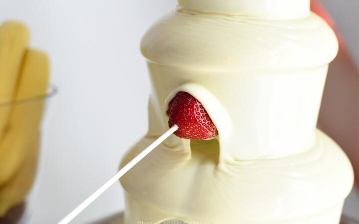 white chocolate fountain with a strawberry on a skewer dipping into the fountain