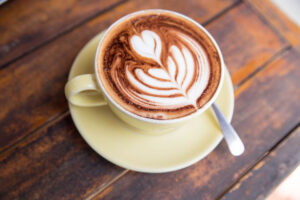 espresso drink with latte art in yellow cup and saucer on a wood table