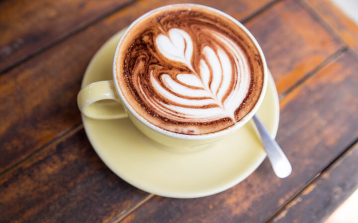 espresso drink with latte art in yellow cup and saucer on a wood table