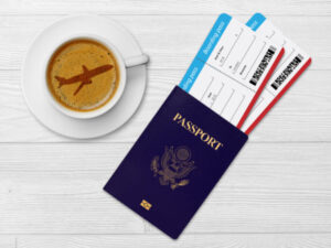 coffee in cup and saucer with airplane latte art, passport with 2 plane tickets next to it on table top