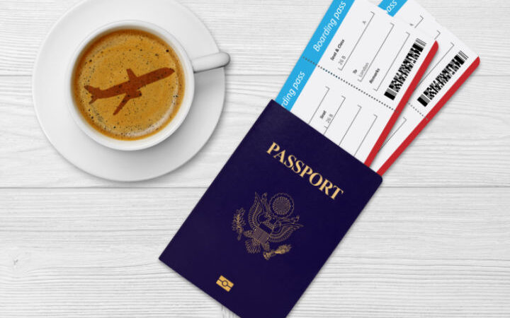 coffee in cup and saucer with airplane latte art, passport with 2 plane tickets next to it on table top