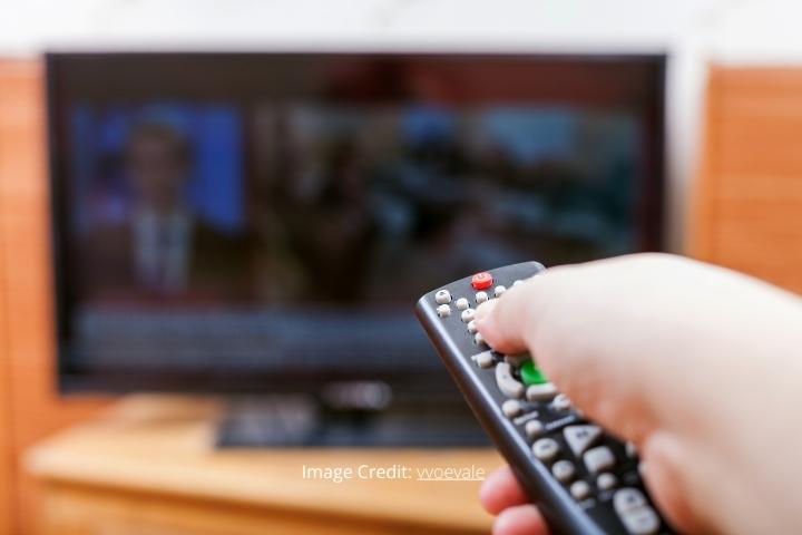 hand switches on TV with news with remote control