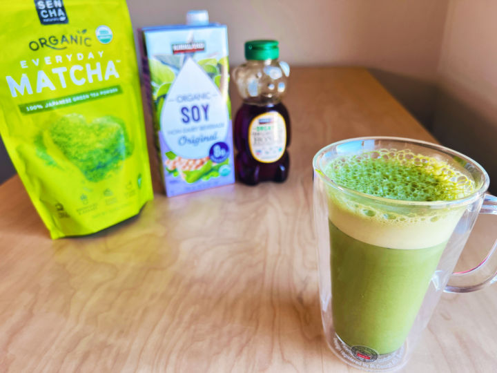 glass of iced matcha latte with background ingredients - matcha powder, soy mok, and honey